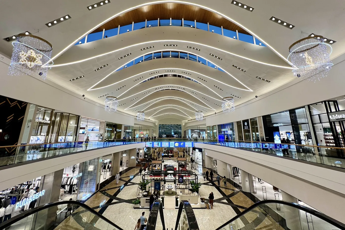 Techo curvo, atrio abierto, escaparates y escaleras mecánicas dentro de Mall of Oman, Mascate.