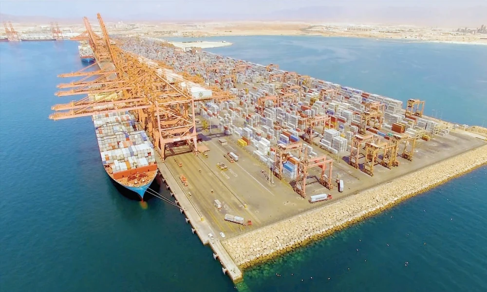 Vista aérea diurna del puerto de Salalah, Omán, con un buque de carga, grúas naranjas y una terminal de contenedores.
